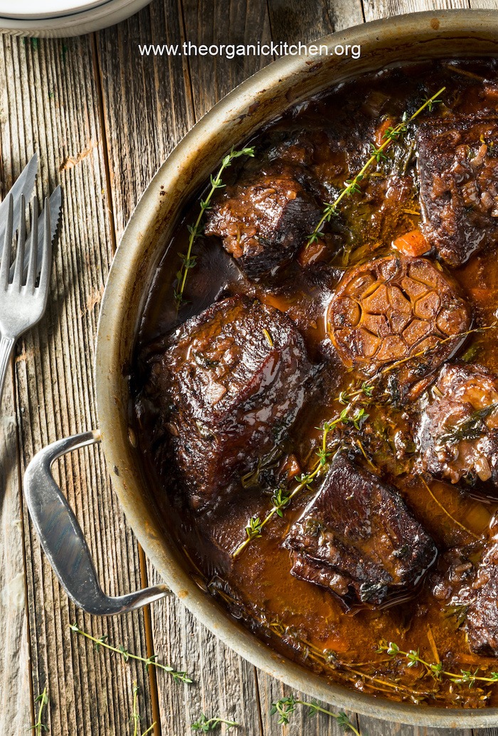 Tender Braised Short Ribs garnished with thyme in a pot on a wooden table