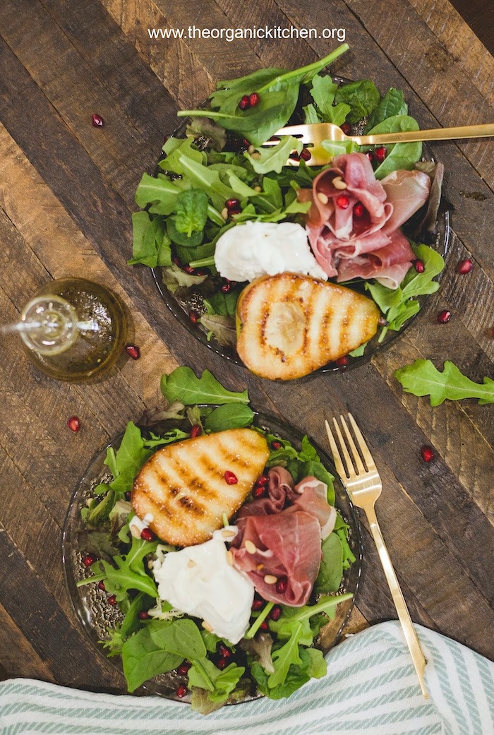 Two plates of Grilled Pear and Prosciutto Salad with gold forks and green and white dish towel at bottom of frame
