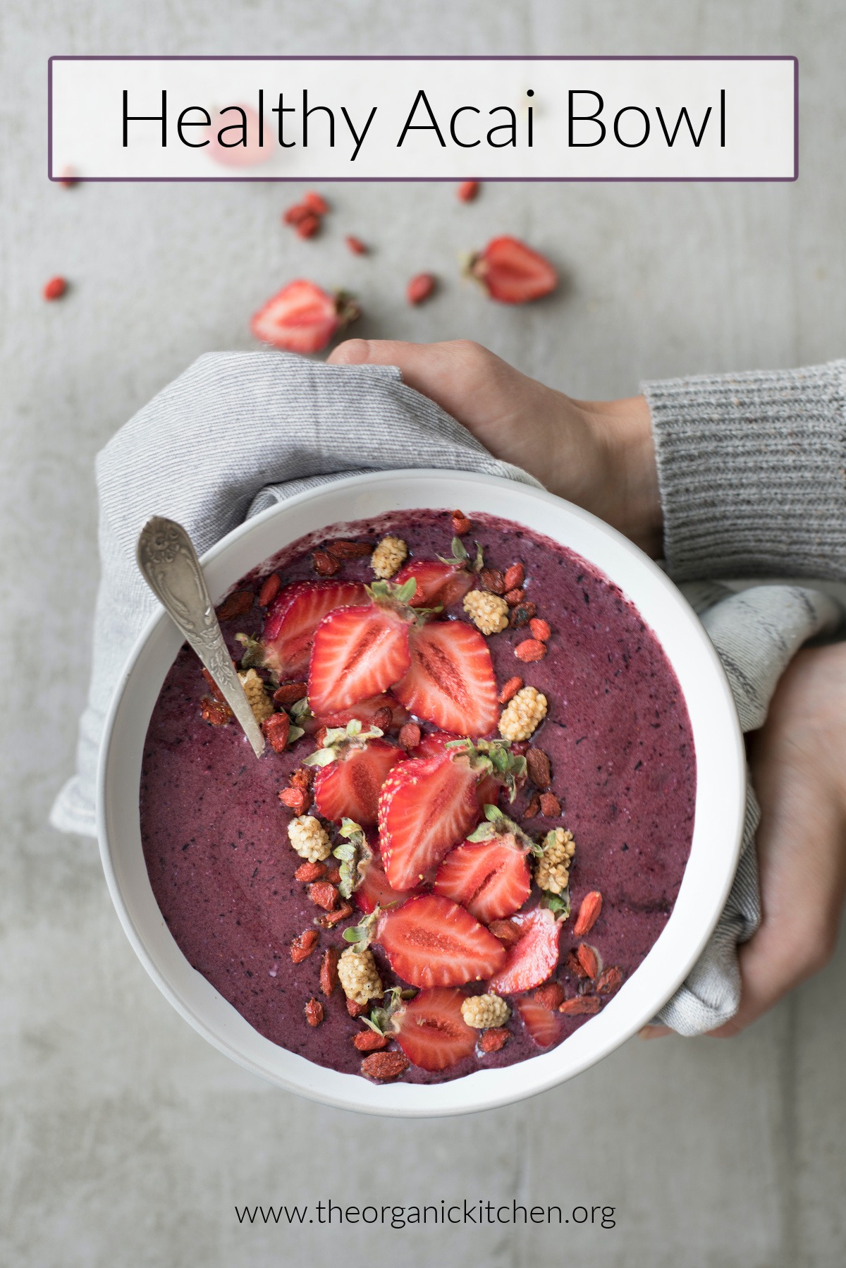 A woman's hands holding a Healthy Açaí Smoothie Bowl with cut strawberries on top