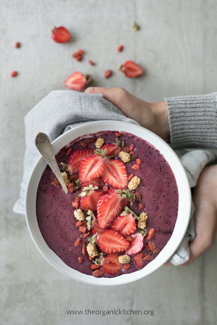 A woman's hands holding a Healthy Açaí Smoothie Bowl with silver spoon