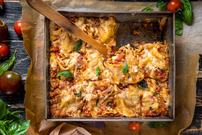 A tin baking pan filled with Traditional Italian Lasagna on a rustic dark wooden table