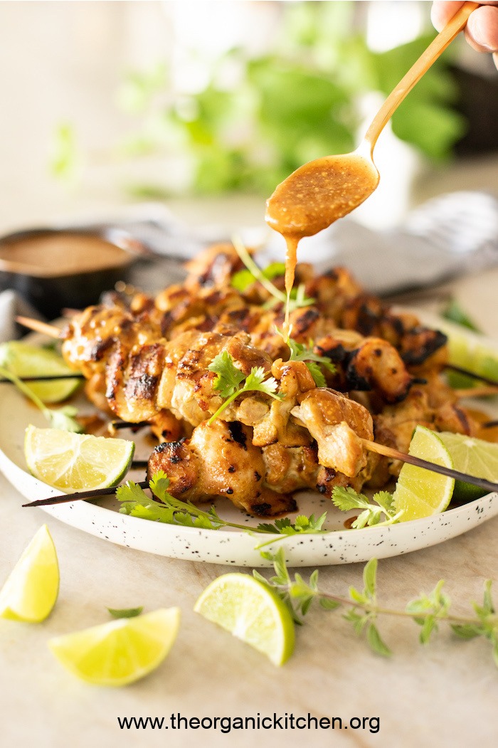 Skewers of Chicken Satay being drizzled with Sweet and Spicy Peanut Sauce