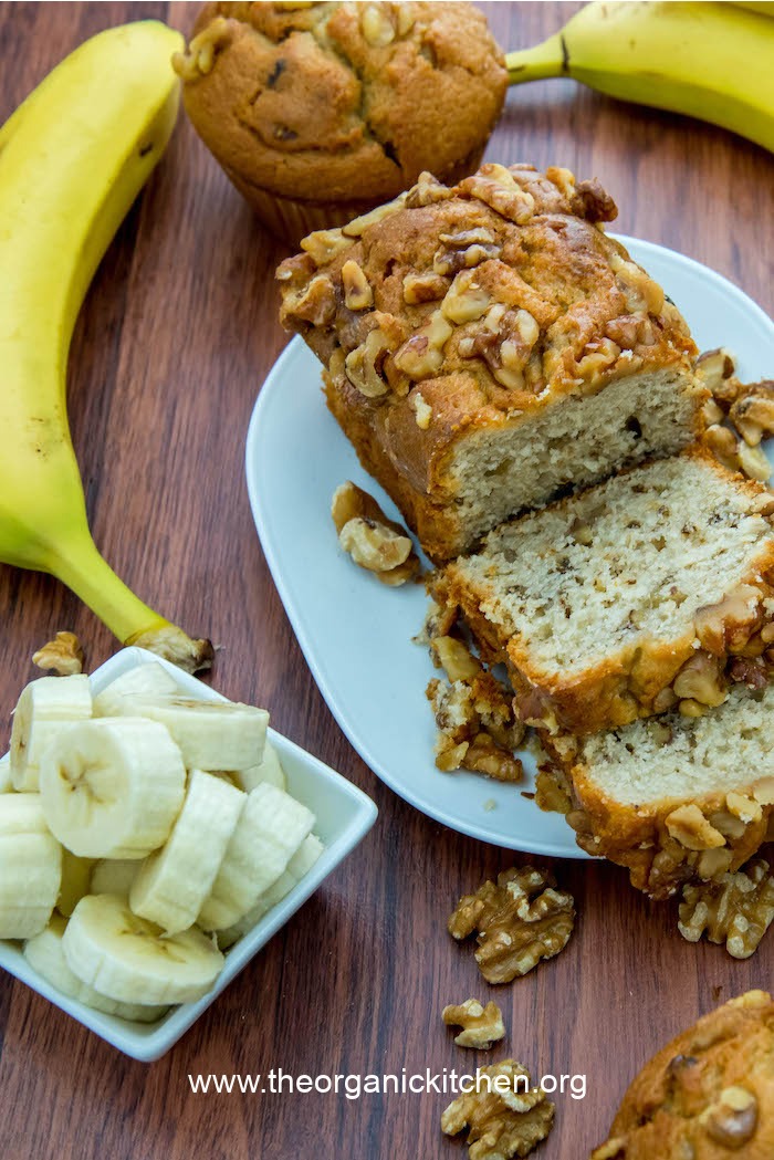 Banana Nut Bread or Muffins (gluten free option) on white plate surrounded by sliced bananas and walnuts
