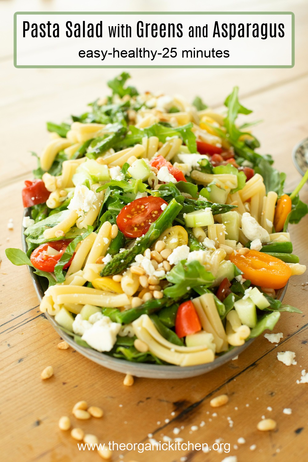 A platter of Pasta Salad with Greens and Asparagus garnished with pine nuts and feta