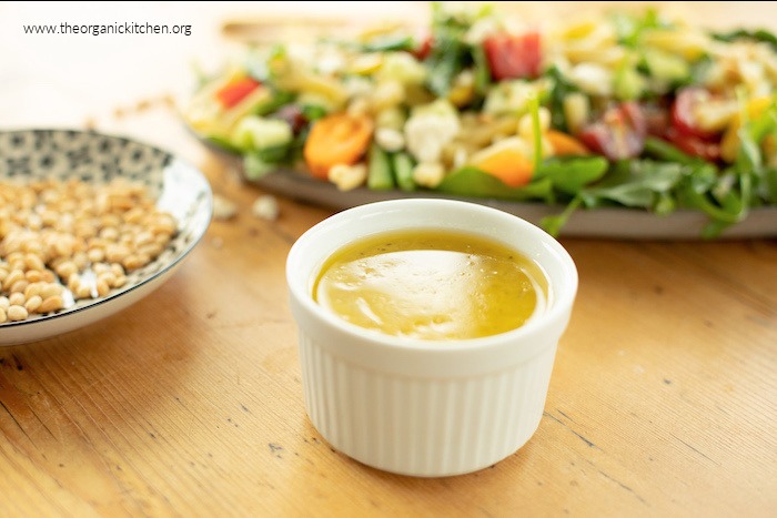 A white ramekin with lemon vinaigrette for Pasta Salad with Greens and Asparagus