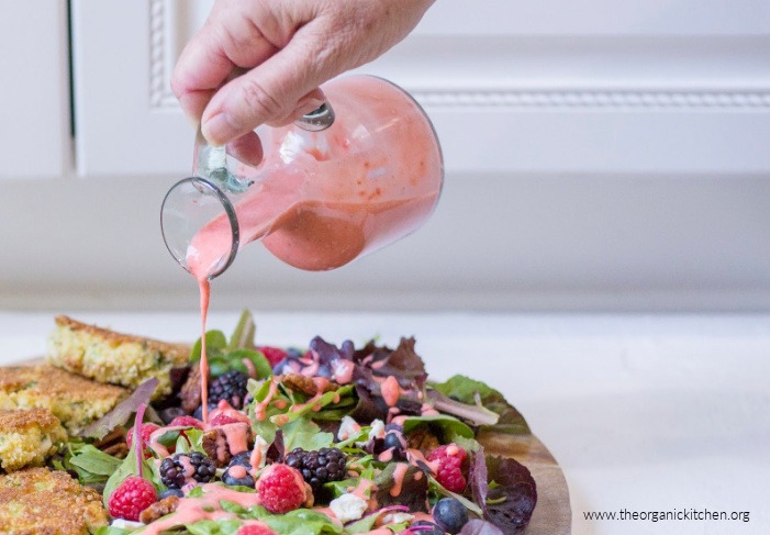 A bottle of Creamy Strawberry Vinaigrette - Whole30/Paleo being poured onto a fresh berry salad 