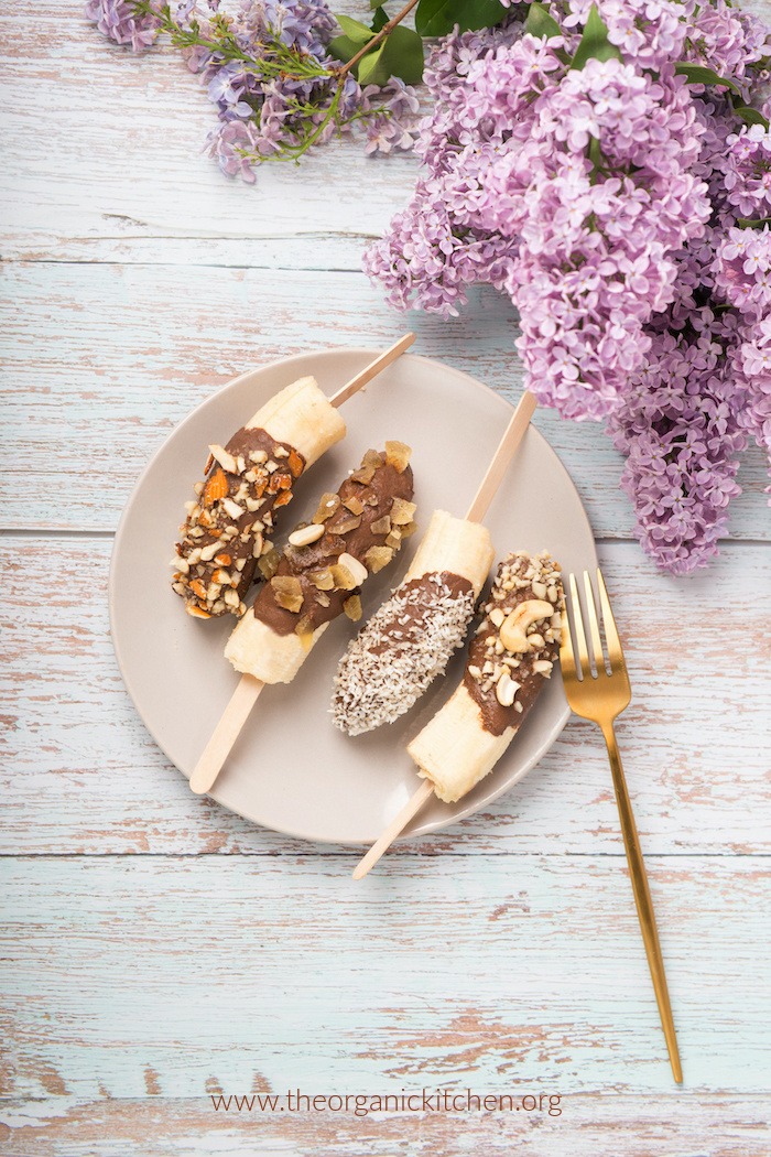 Chocolate Dipped Frozen Bananas on white plate with fresh lilacs on table