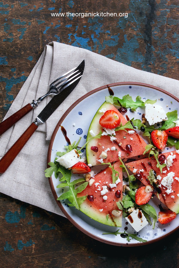 Watermelon Salad garnished with feta and arugula on blue plate with napkin and a knife and fork