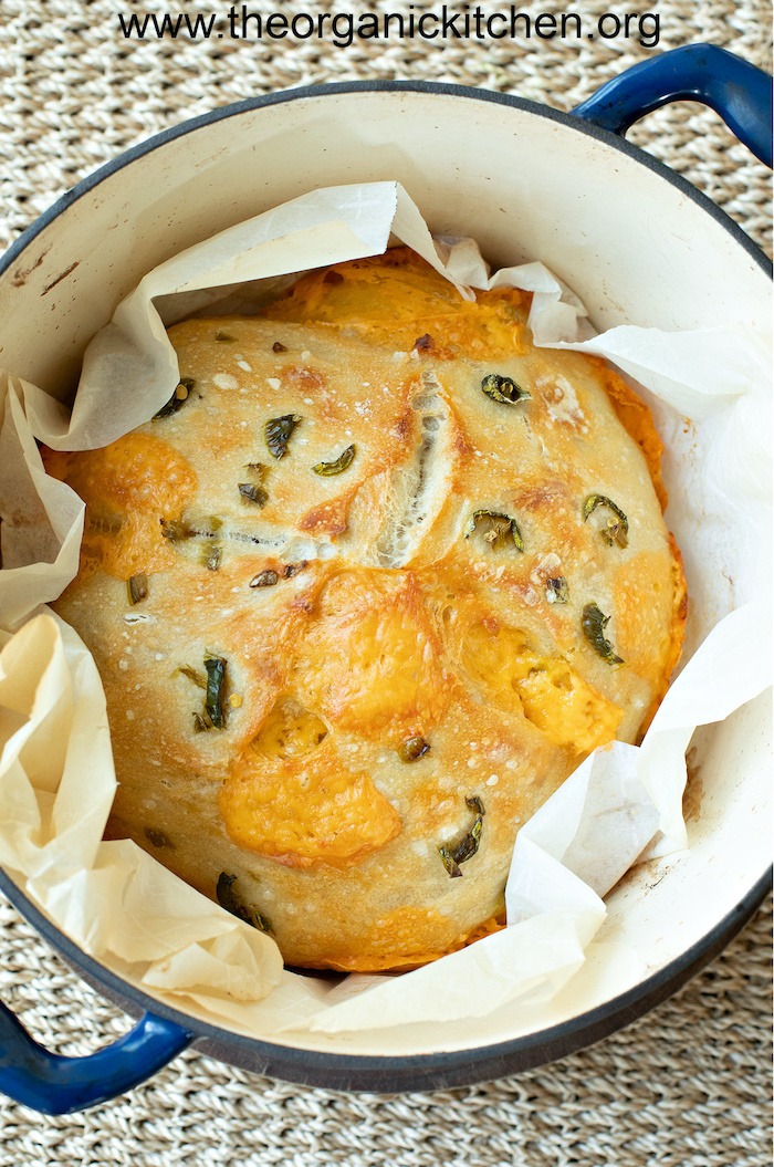 A loaf of baked Cheddar Jalapeno Sourdough bread set on parchment paper in a Dutch oven