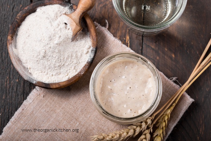 Sourdough starter and flour in bowls on wood table