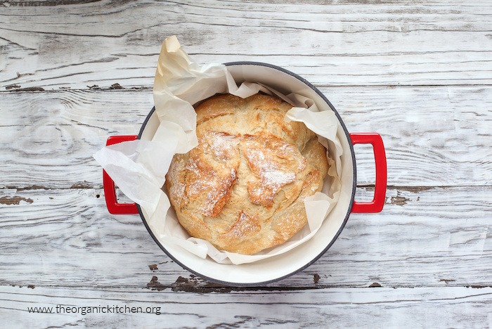 A baked loaf of sourdough in a Dutch oven on white table