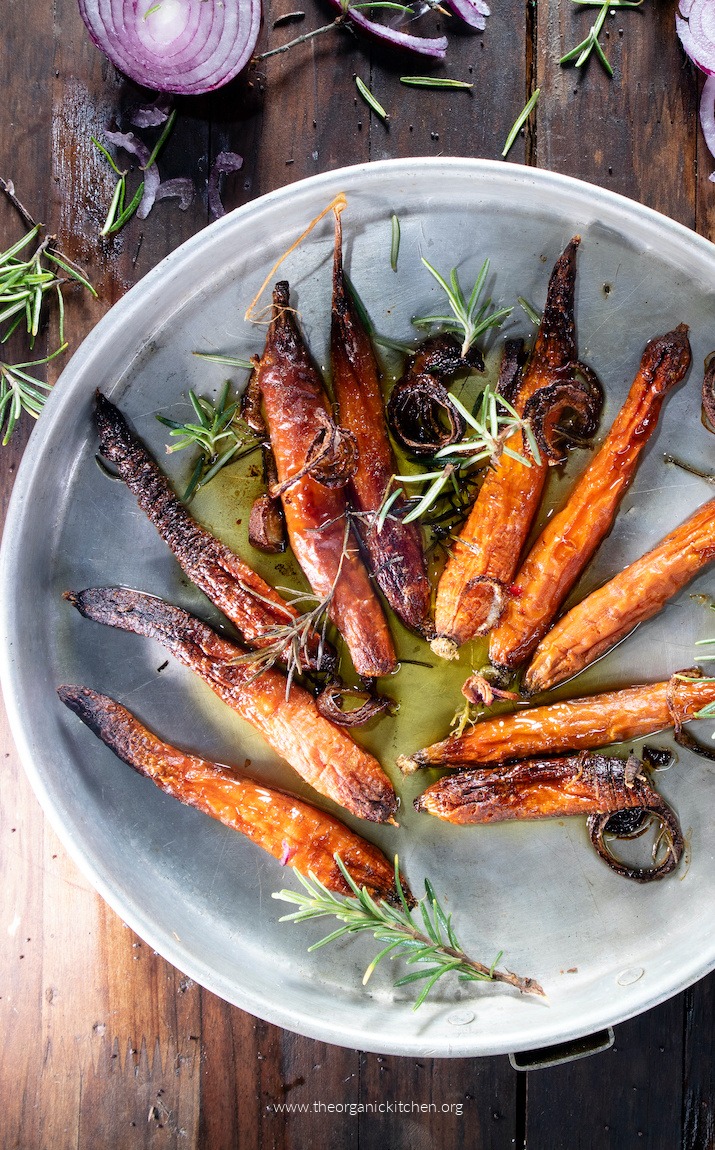Easy Roasted Baby Carrots garnished with herbs on dark wood table