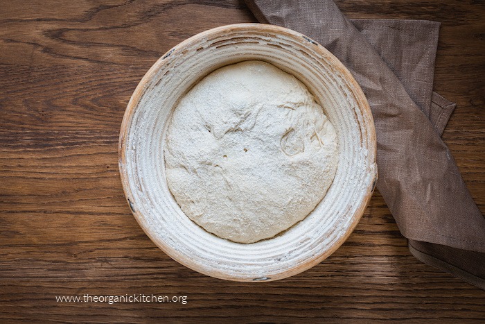 A white bowl filled with rising bread dough on wood table