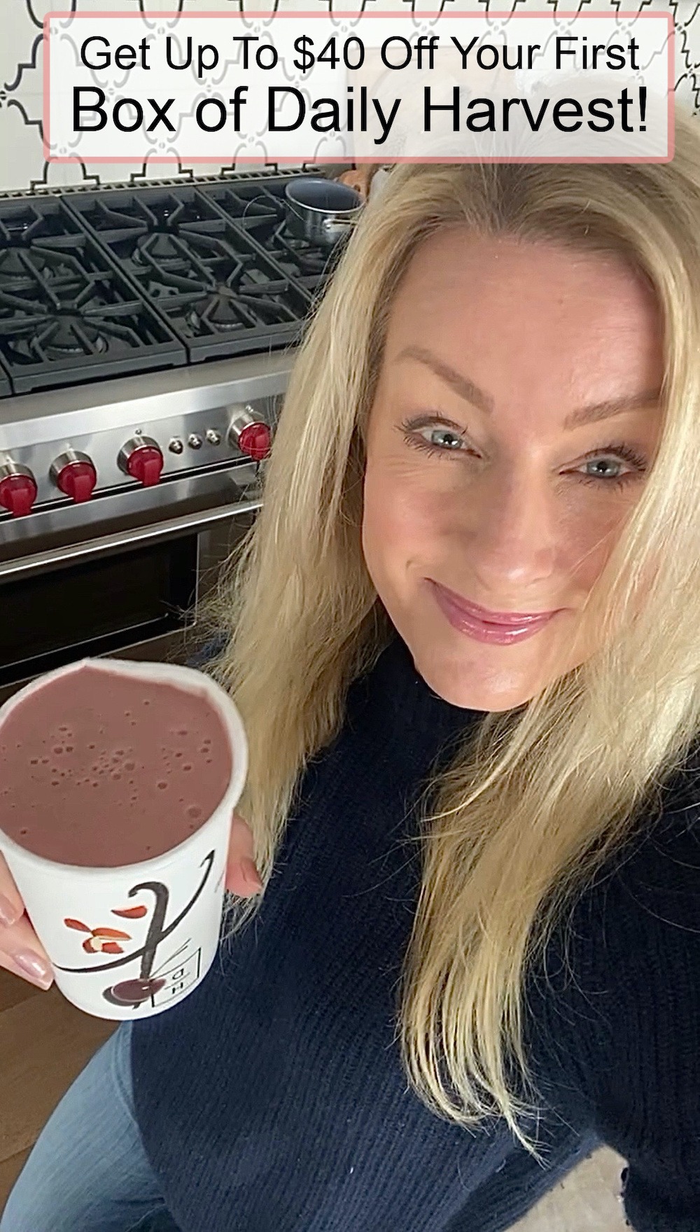 A blonde woman in blue sweater holding a pink smoothie in a Daily Harvest cup.