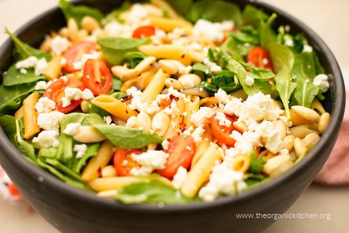 Penne Pasta with Tomatoes and Baby Arugula garnished with Marcona almonds and feta cheese in a black bowl 