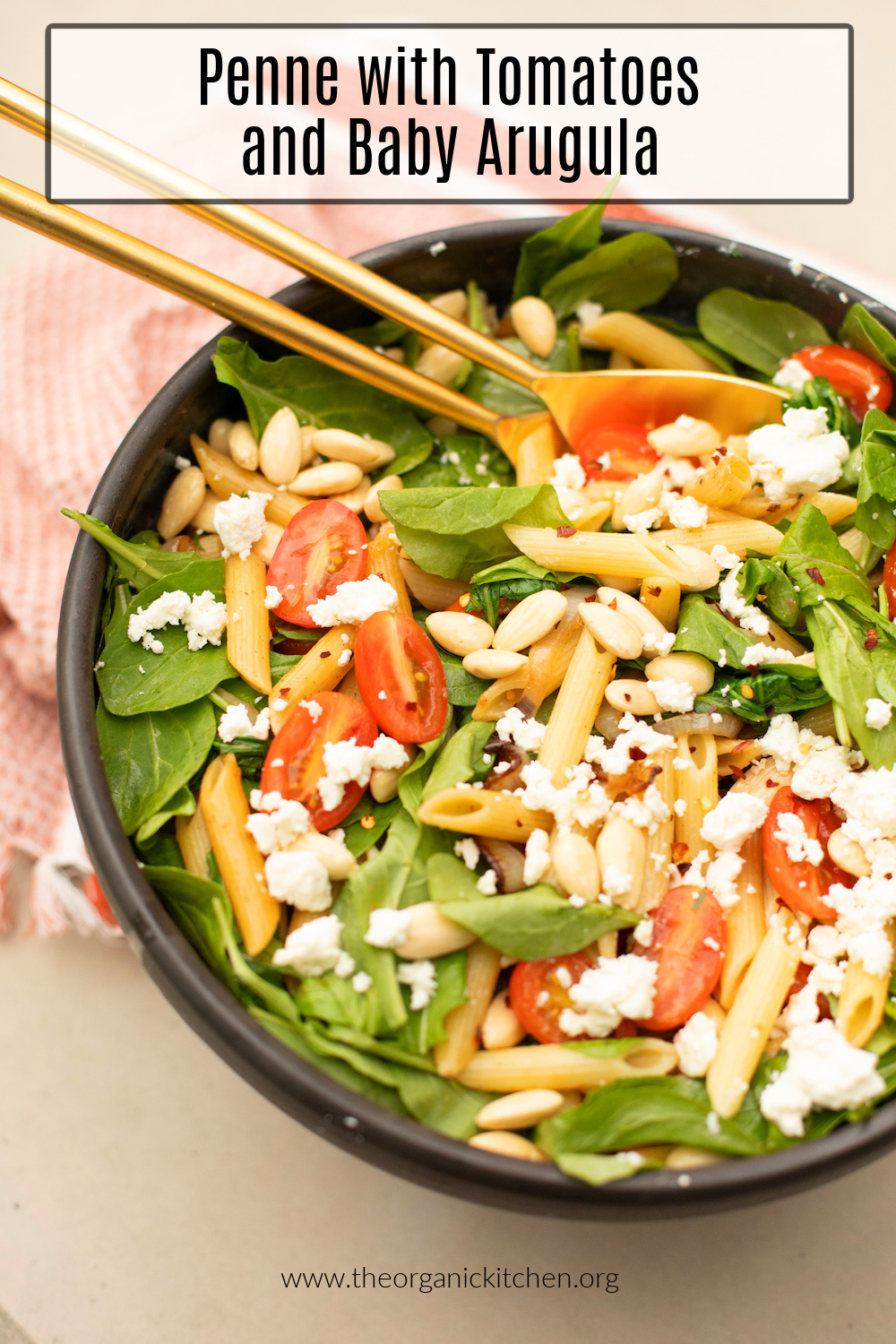 Penne Pasta with Tomatoes and Baby Arugula in a black bowl with gold serving spoons