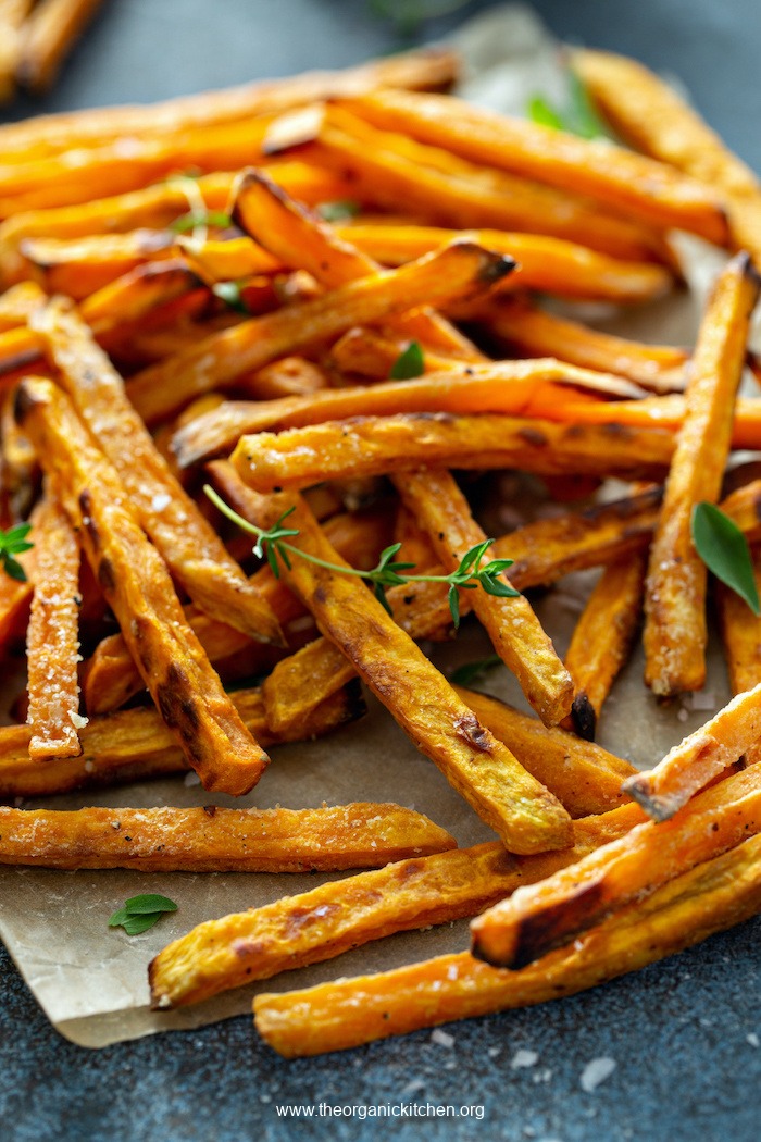 A stack of Air Fryer Sweet Potato Fries (Whole30) on parchment with a garnish of sea salt and thyme