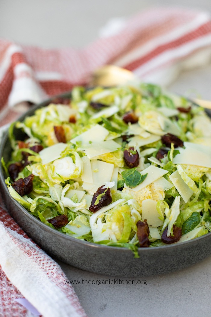 Shaved Brussels Sprouts and Date Salad with Shaved Parmesan in grey bowl on cement table