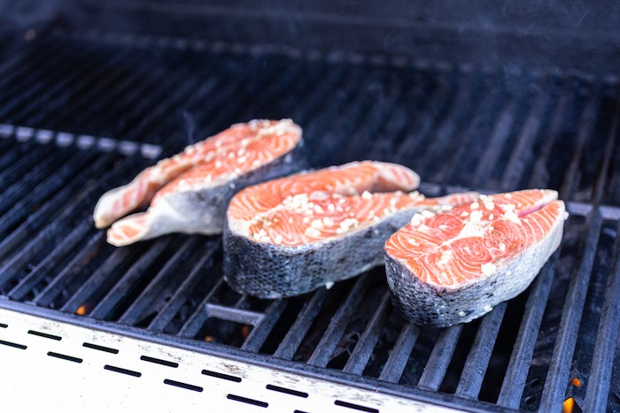 Three salmon steaks seasoned with sea salt and pepper on the bBQ grill