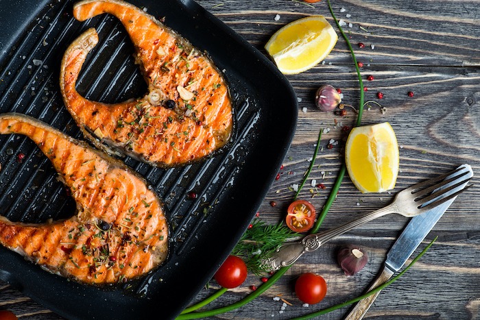 Grilled red fish steaks salmon on the grill pan surrounded by lemon wedges and cherry tomatoes