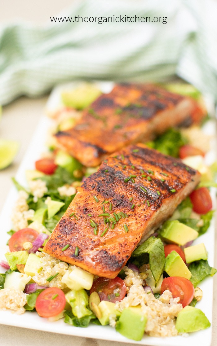 Blackened salmon garnished with chives atop a fresh romaine salad on white plate
