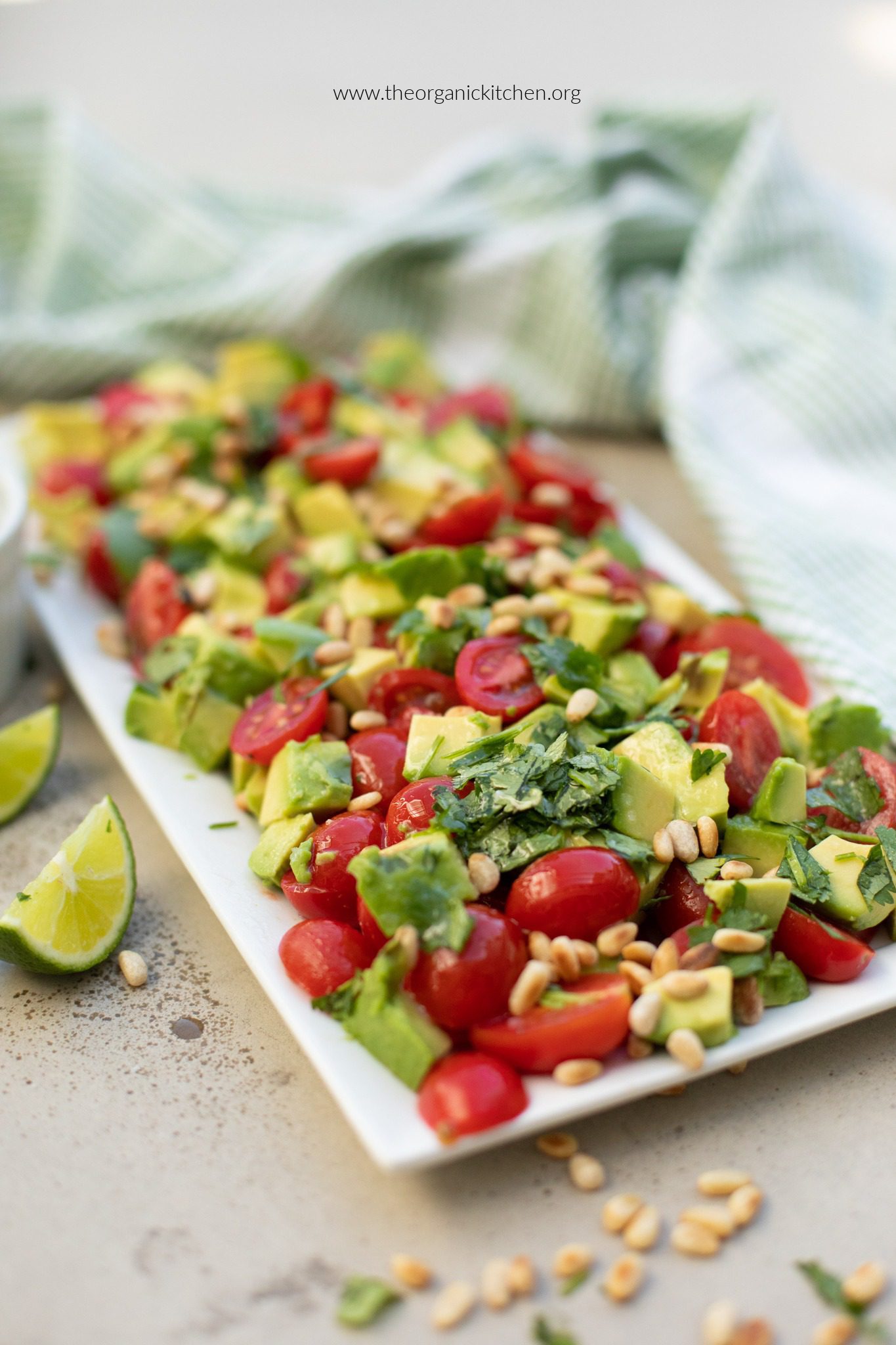 Tomato Avocado Salad (Whole30) garnished with cilantro and lime wedges on white plate with green dish towel in the background
