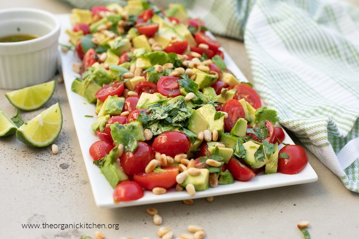 Tomato and Avocado Salad on white platter surrounded by lime wedges and a green and white dish cloth