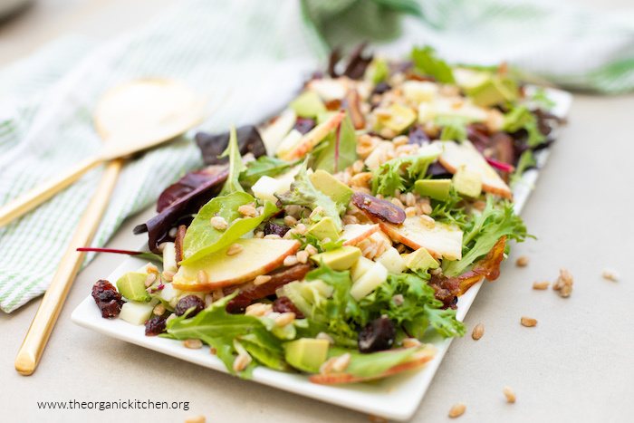 Apple and Farro Salad on white platter with gold serving spoons