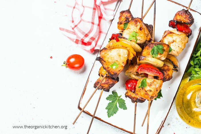 Grilled Greek Chicken Kabobs (Whole30-Keto) garnished with cherry tomatoes and herbs on white plate with red and white dish towel in background