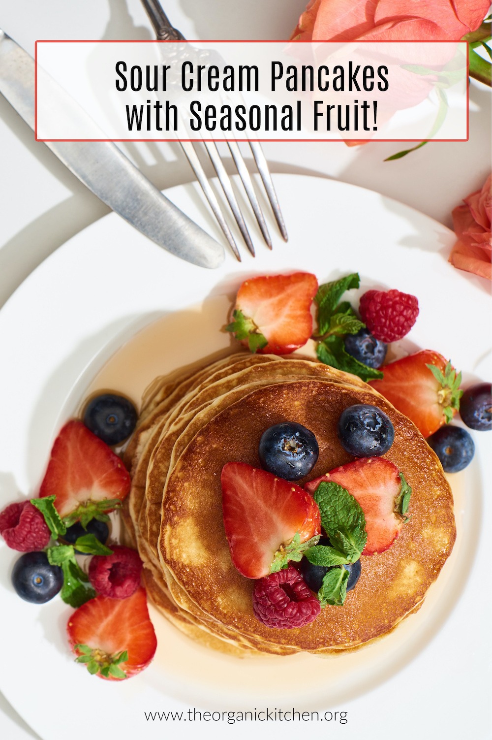 Sour Cream Pancakes with Seasonal Fruit on a white plate with silver fork and knife in upper left of frame