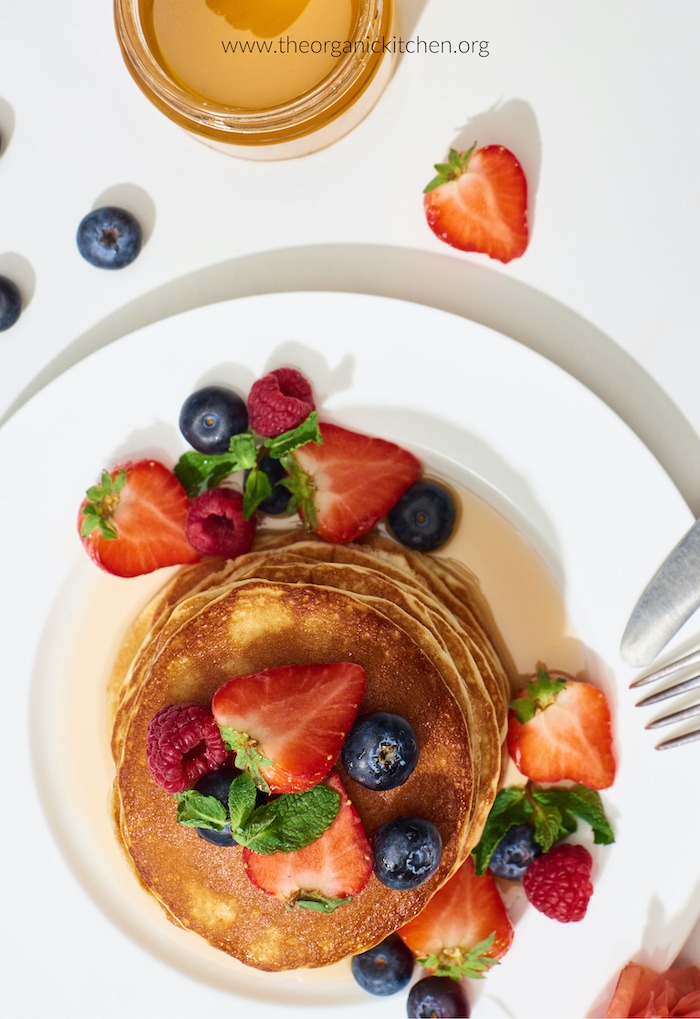 Sour Cream Pancakes with Seasonal Fruit on white plate with small jar of maple syrup