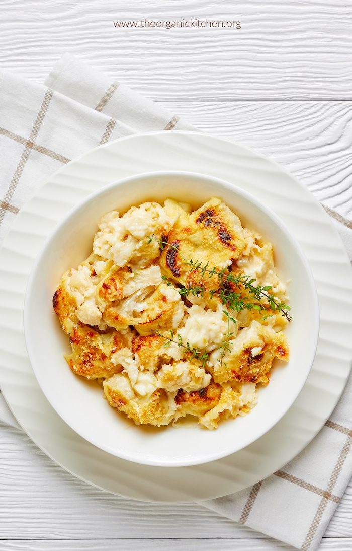 Cauliflower with Three Cheese Sauce in white bowl set on white plate with dish towel