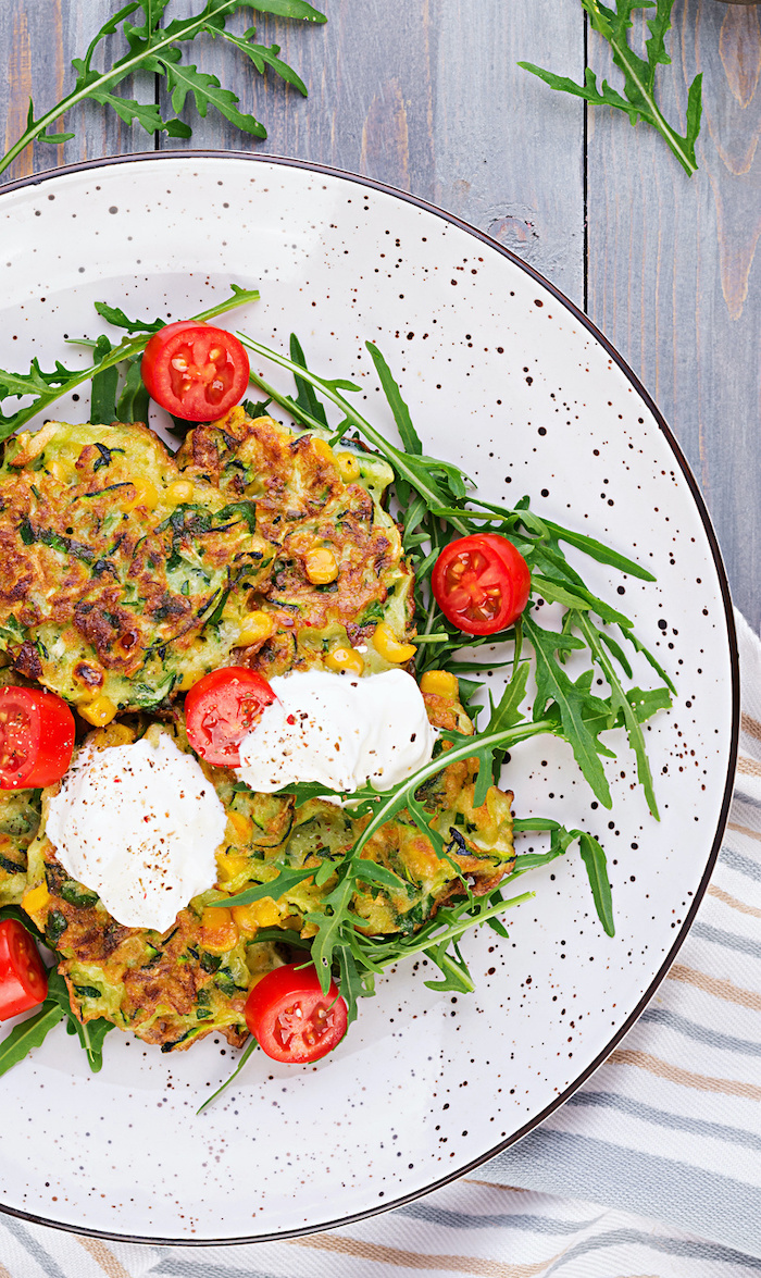 Top view of Zucchini-Corn Fritters with sour cream and tomatoes served on arugula,