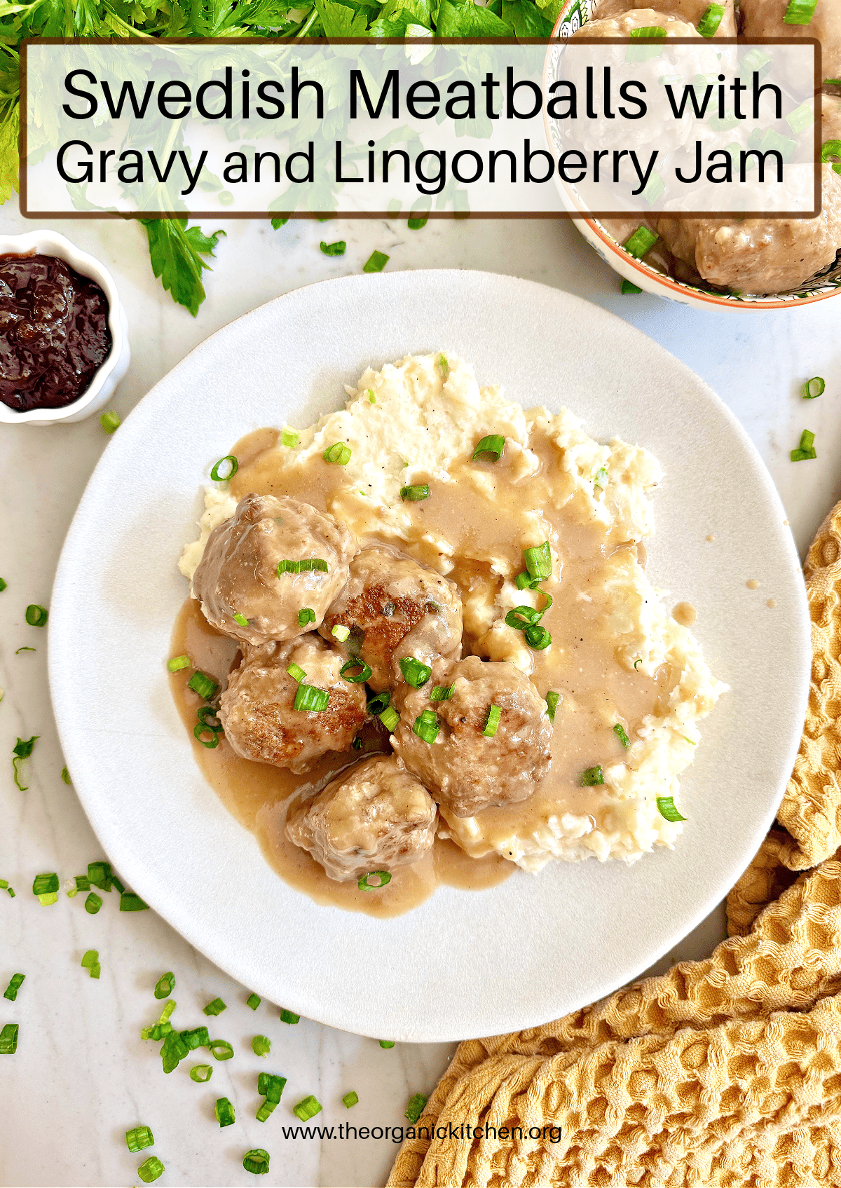 Swedish Meatballs with Lingonberry Jam and Mashed Potatoes on white plate surrounded by a bowl of jam, a yellow dish towel and a bowl of meatballs