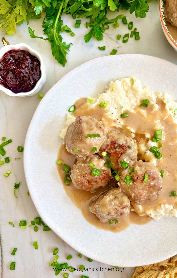 Meatballs with Lingonberry Jam and Mashed Potatoes on white plate with parsley above and a bowl of jam to the side