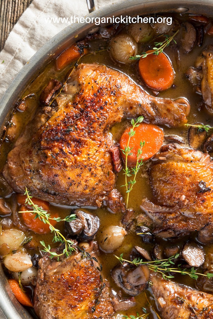 A close up flay lay of Coq Au Vin (Chicken in Red Wine) garnished with thyme