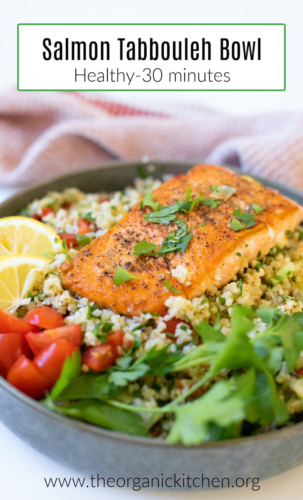 A colorful Salmon Tabbouleh Bowl in grey dish, surrounded by lemon wedges, parsley, and sliced tomatoes