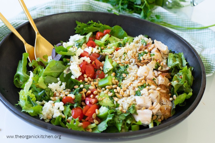 A beautiful green salad in black bowl with gold serving spoons