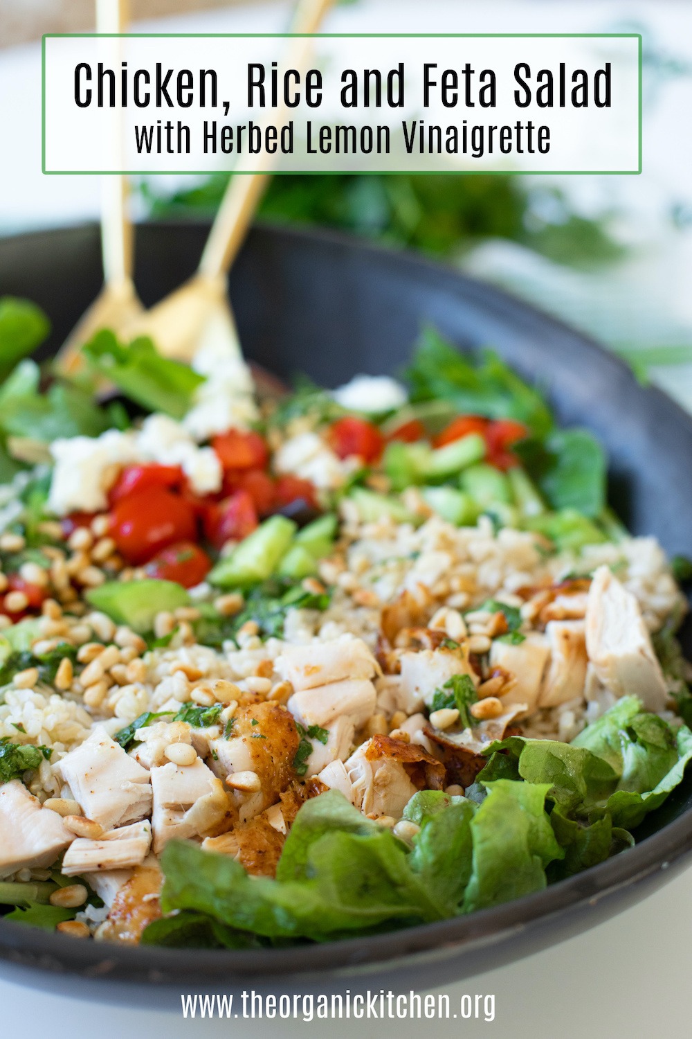 Chicken, Rice and Feta Salad in black bowl with gold serving spoons in background