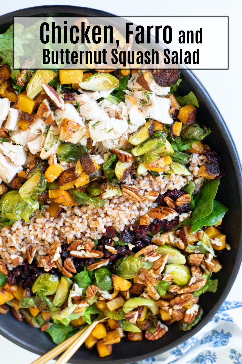 The colorful Chicken, Farro and Roasted Butternut Squash Salad in black bowl with gold serving utensils