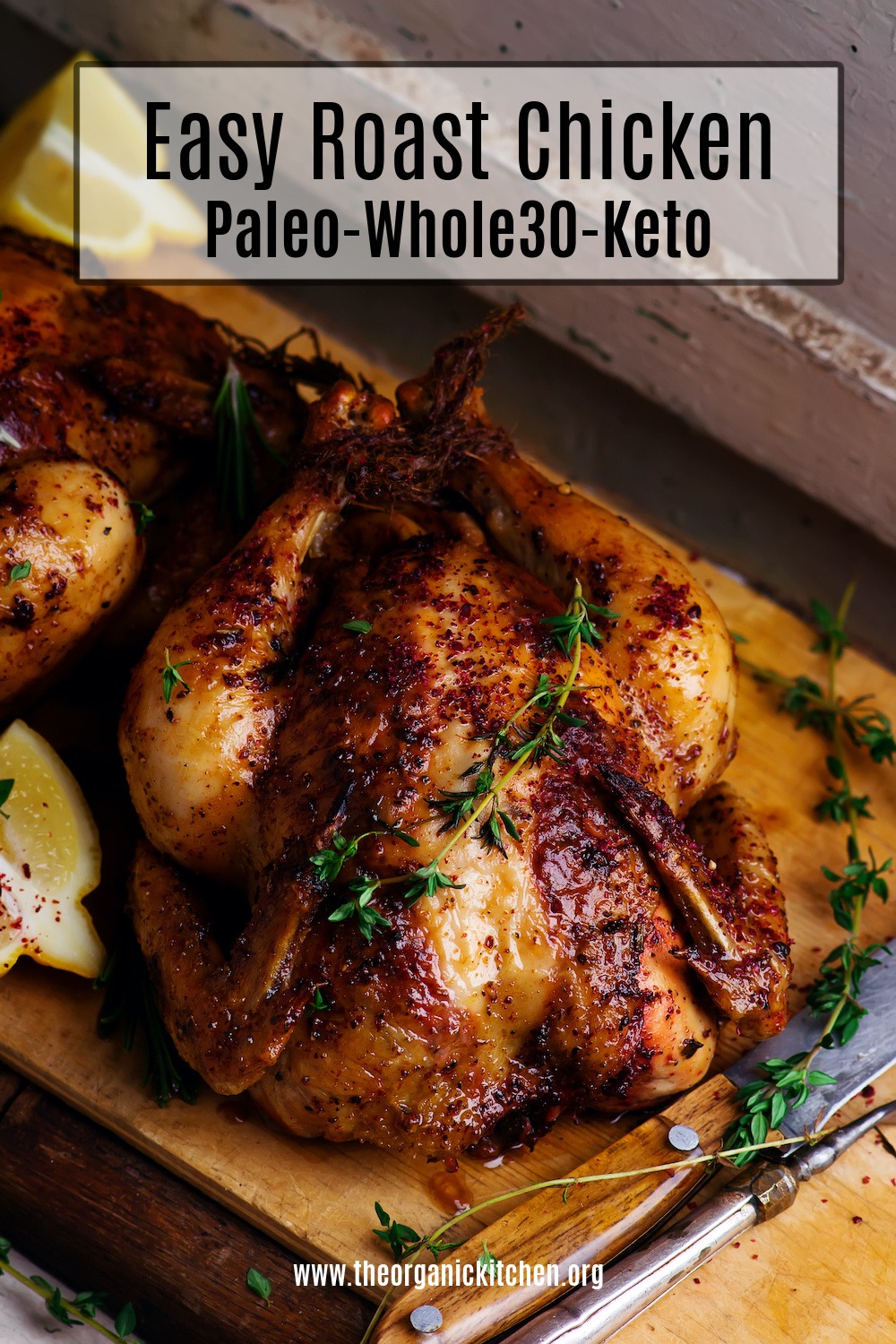 Easy Roast Chicken- Whole30/Keto garnished with thyme, on wood board surrounded by lemon wedges