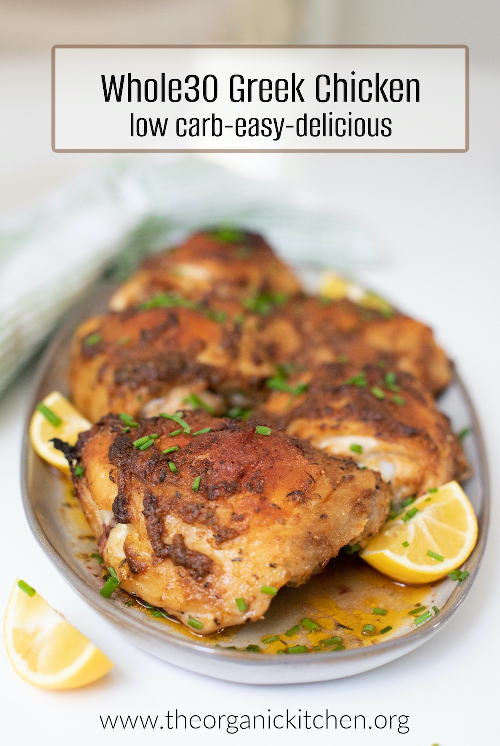 Whole30-Keto Greek Chicken Thighs garnished with lemons and chives on a grey plate