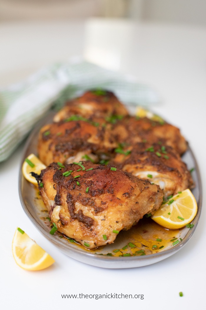 Greek Chicken Thighs with lemon wedges on grey plate with green and white dish towel in background.