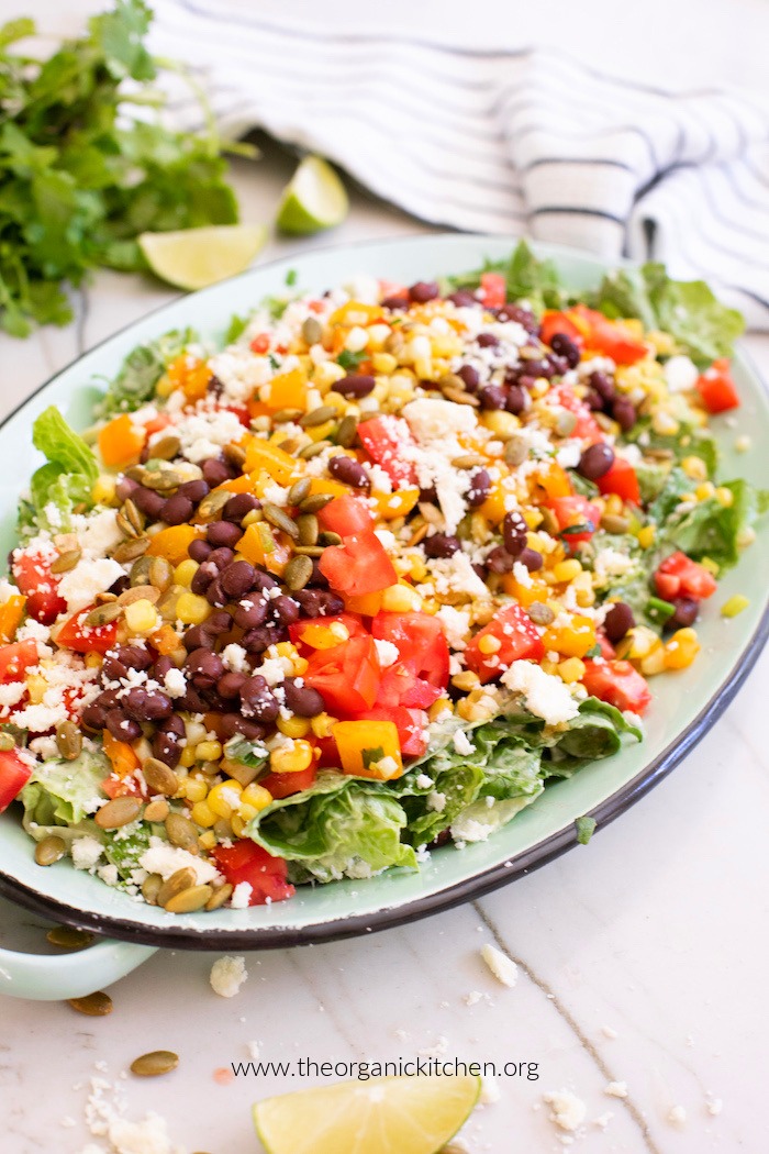 Chopped Mexican Salad with Creamy Avocado Ranch on green platter with lime wedge in the foreground and cilantro and limes in the background