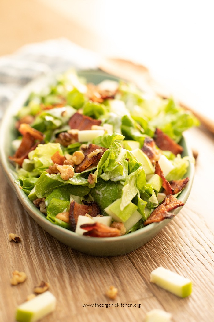 Green Salad with Apples and Bacon (Whole30) on green platter atop a wood table with scattered walnuts and apples