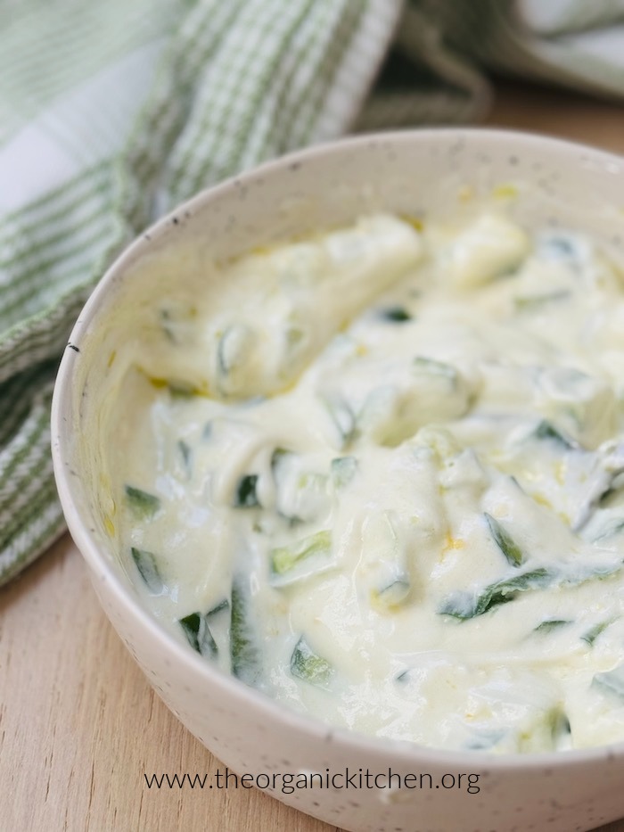 Tzatziki sauce in a white bowl with green and white dish towel in the background