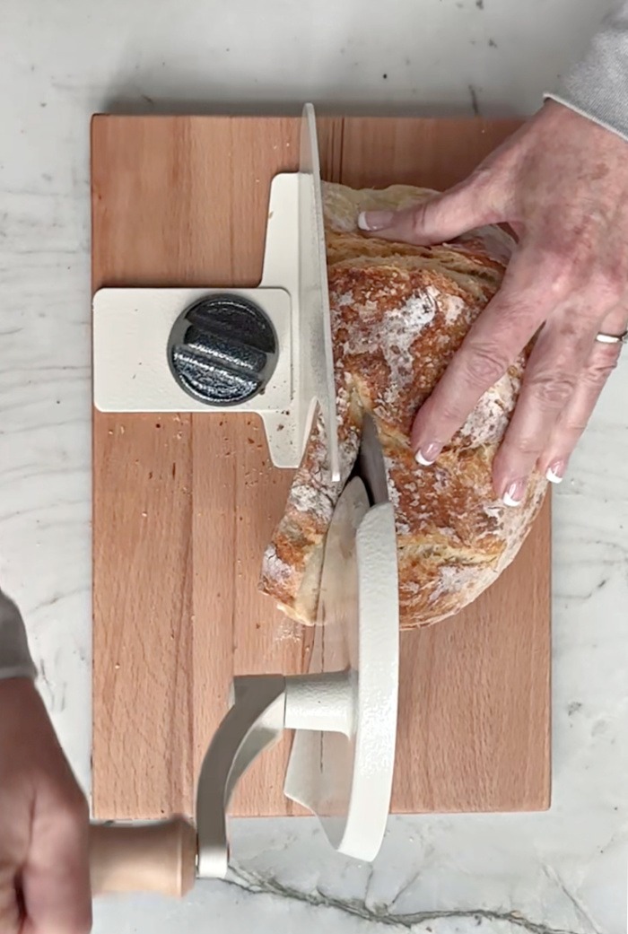 A woman's hands putting a loaf of sourdough through a bread slicer