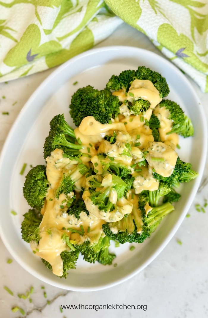 Steamed broccoli with cheese sauce on white plate set on marble surface