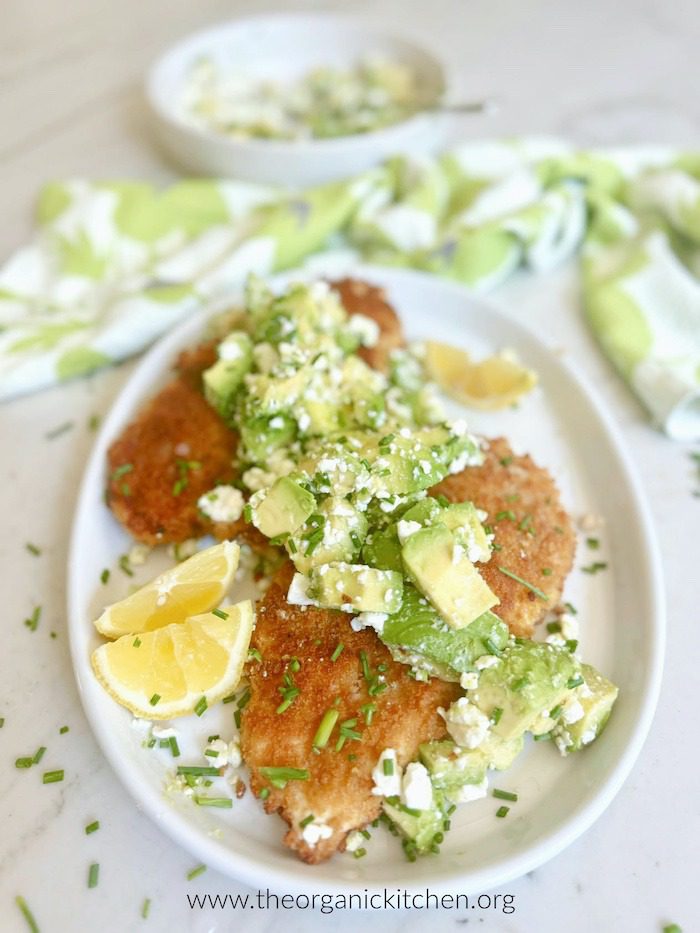 Crispy Chicken with Avocado Feta Salad Crispy Chicken with Avocado Feta Salad on white plate with bowl of salad and dish towel in the backround