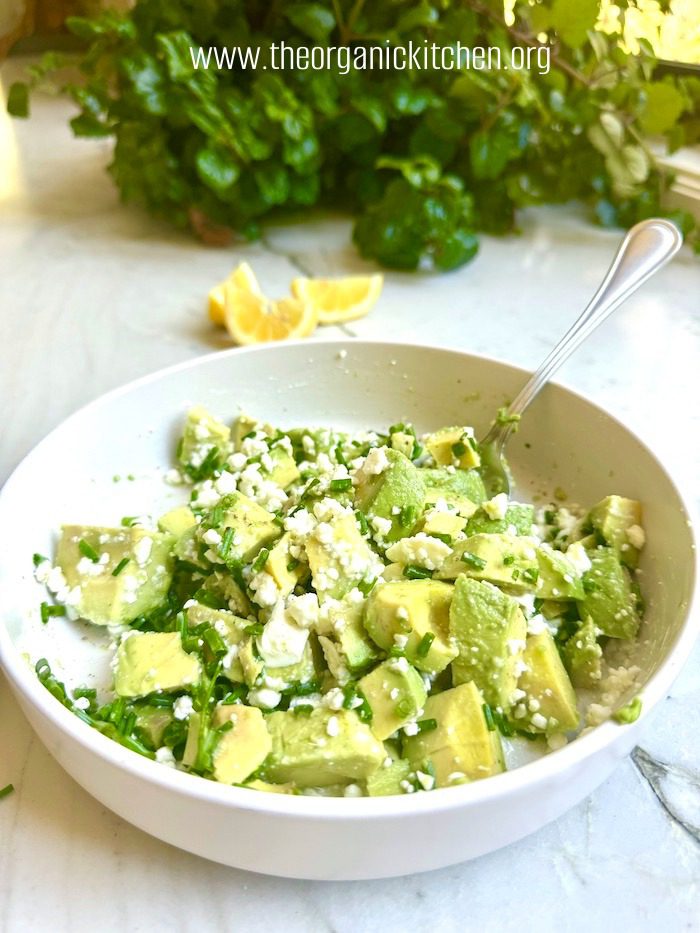 Crispy Chicken with Avocado and Feta Salad A white bowl filled with avocado and feta salad garnished with chives